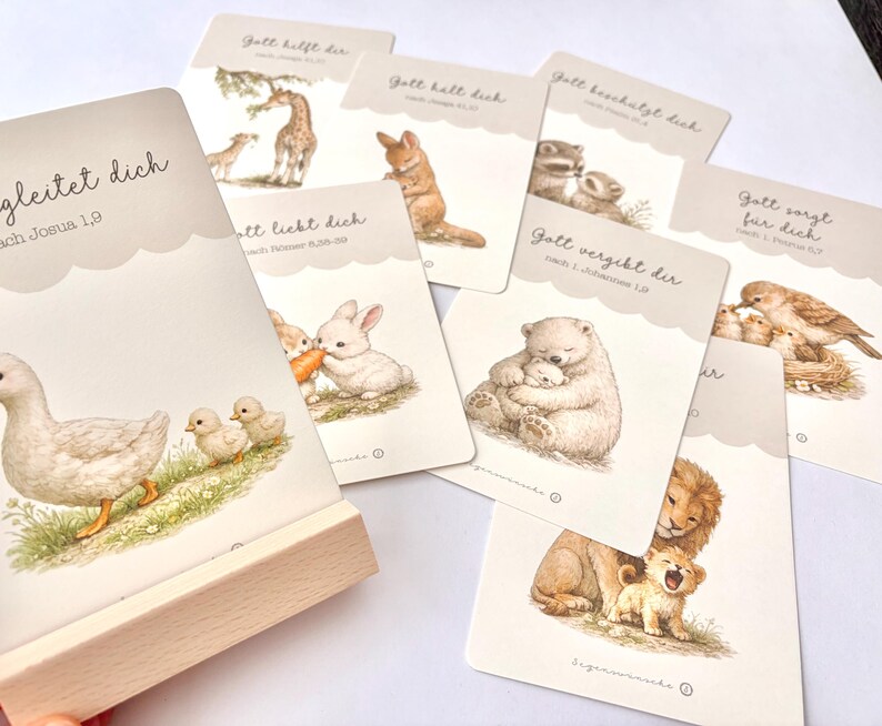 May include: A set of illustrated cards with animal images and German text. The cards feature a duck with ducklings, a giraffe, a rabbit, a bear, a lion, and other animals. The cards are displayed with a wooden holder.