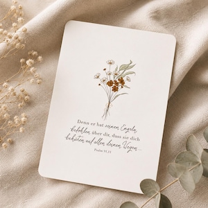 Könnte beinhalten: Eine cremefarbene Karte mit einer floralen Illustration und Text. Der Blumenstrauß zeigt weiße und braune Blüten mit grünen Blättern. Der Text lautet: "Denn er hat seinen Engeln befohlen über dir, dass sie dich behüten auf allen deinen Wegen... Psalm 91,11."