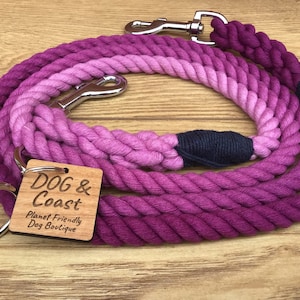 Pode incluir: Uma trela para cães de corda de algodão rosa degradê com um clipe prateado e uma etiqueta de madeira que diz "DOG & Coast Planet Friendly Dog Boutique".