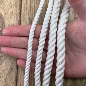 May include: Four different sizes of white cotton rope, displayed on a hand.