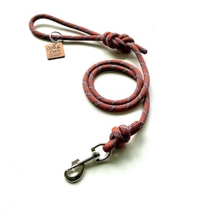May include: A dog lead made of orange and grey speckled rope with a silver metal swivel snap hook at one end. The lead features two knots and a square wooden tag attached to a metal ring, engraved with the text DOG & COAST Planet Friendly Dog Boutique.