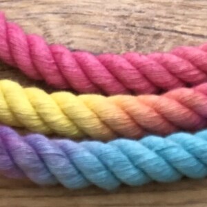 May include: A multi-colored rope with a rainbow gradient of pink, yellow, green, and blue. The rope is made of cotton and is twisted together.
