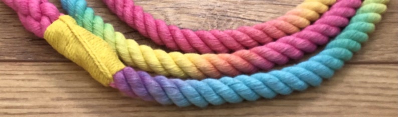 May include: A multi-colored rope with a rainbow gradient of pink, yellow, green, and blue. The rope is made of cotton and is twisted together.