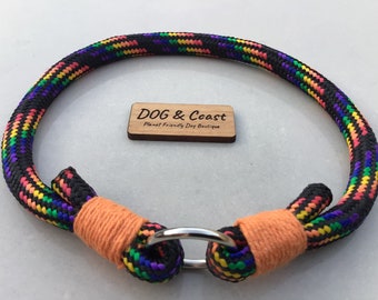 May include: A dog collar made of black rope with rainbow-colored accents. The collar has orange accents and a silver metal ring. A wooden tag with the text "DOG & Coast" is also present.