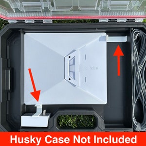 May include: A white device with a black power cord and a white power adapter in a black carrying case. The case is open and the device is sitting inside. The text "Husky Case Not Included" is printed on the bottom of the image.