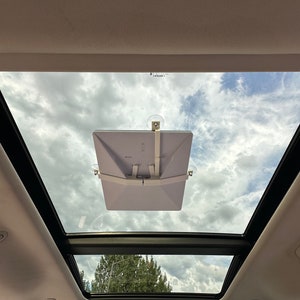 Peut inclure: Une tablette blanche fix&eacute;e au toit ouvrant d'une voiture &agrave; l'aide de ventouses. La tablette est inclin&eacute;e vers l'avant de la voiture. Le toit ouvrant est ouvert, r&eacute;v&eacute;lant un ciel bleu avec des nuages blancs.