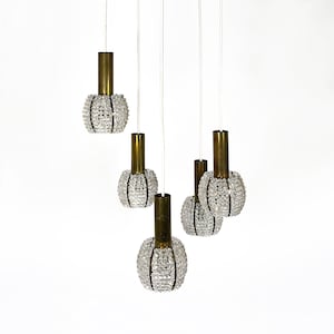 Op de afbeelding: Een messing en kristallen kroonluchter met vijf lampen. De kroonluchter heeft een modern ontwerp en is perfect voor een eetkamer of woonkamer.