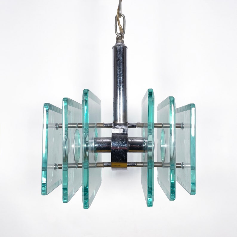 Peut inclure: Un lustre moderne en chrome et en verre avec un design g&eacute;om&eacute;trique. Le lustre est compos&eacute; de plusieurs panneaux rectangulaires en verre suspendus &agrave; une tige en chrome.