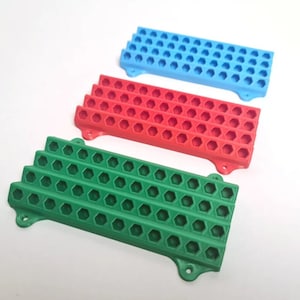 May include: Three plastic trays with hexagonal compartments. The trays are stacked on top of each other. The top tray is blue, the middle tray is red, and the bottom tray is green.