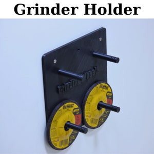 May include: A black wall-mounted grinder holder with three metal pegs. Two Dewalt grinding wheels are attached to the pegs. The holder has the text "Grinding Wheels" printed on it.