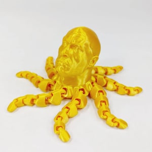 Könnte beinhalten: Ein gelber 3D-gedruckter Tintenfisch mit einem menschlichen Kopf. Der Tintenfisch hat acht Tentakel und der Kopf ist mit Gesichtszügen detailliert.