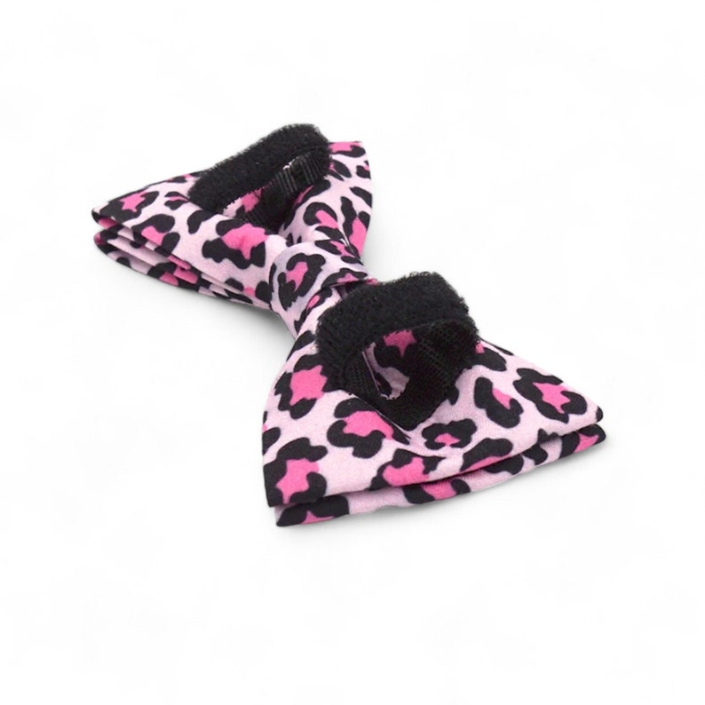 May include: Pink and black bow tie with a leopard print pattern. The bow tie has an adjustable strap.