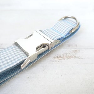 Op de afbeelding: Een lichtblauwe en witte gingham hondenriem met een zilveren gesp en een zilveren D-ring.