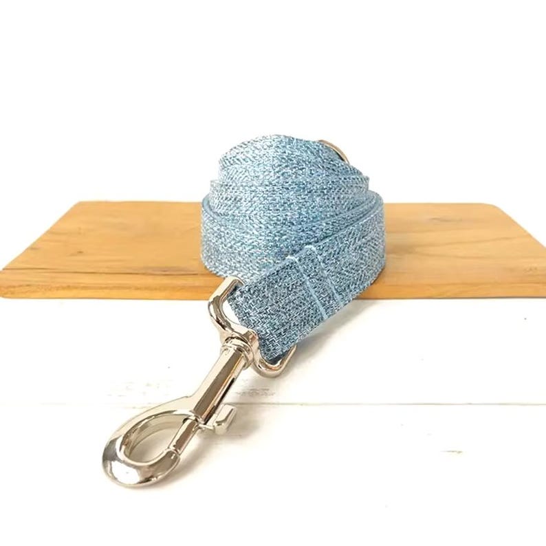 Puede incluir: Una correa para perro de mezclilla azul claro con un clip de metal plateado.