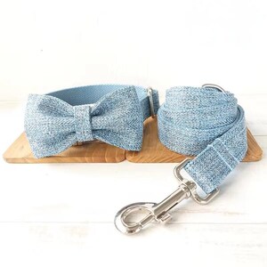 Puede incluir: Un collar para perro de mezclilla azul claro con una pajarita a juego y una correa. La correa tiene un gancho plateado.