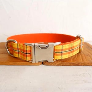 May include: A yellow and orange plaid dog collar with a silver buckle.