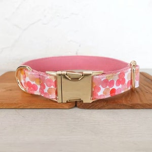 May include: A pink dog collar with a gold buckle and a white background with pink and orange watercolor dots.