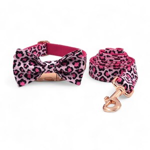 May include: Pink and black leopard print dog collar and leash set with a matching bow tie. The collar and leash have a rose gold buckle and clasp.