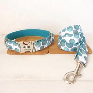 Puede incluir: Un collar de perro azul turquesa con una hebilla plateada y una correa a juego con fondo blanco y lunares azul turquesa. El collar tiene una etiqueta plateada que dice "SCOUT 123-456-7890".