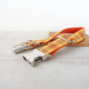 May include: A yellow and orange plaid dog collar with a silver buckle and D-ring.