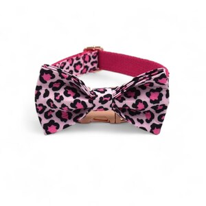 May include: Pink dog collar with a leopard print bow tie. The collar has a rose gold buckle.