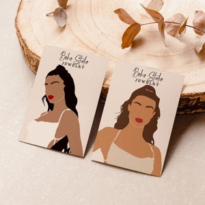 Pode incluir: Dois cart&otilde;es de visita com um design minimalista que apresenta ilustra&ccedil;&otilde;es de mulheres com cabelo castanho e l&aacute;bios vermelhos. O texto nos cart&otilde;es diz "Boho Studio Joias".
