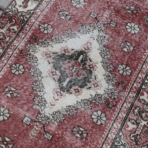 Puede incluir: Una alfombra vintage roja y blanca con un patrón floral descolorido. La alfombra tiene un aspecto desgastado y está hecha de lana.