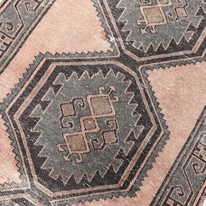 Puede incluir: Una alfombra vintage con un patrón geométrico en tonos marrones, grises y rosas. La alfombra tiene un aspecto desgastado y envejecido, lo que añade carácter.