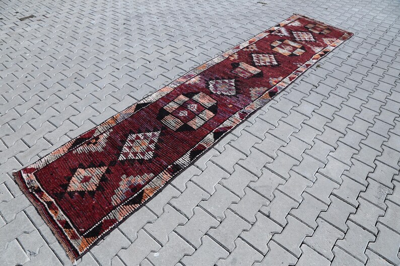 Puede incluir: Una alfombra larga y estrecha de color rojo y crema con un patr&oacute;n geom&eacute;trico. La alfombra tiene un patr&oacute;n de diamantes con acentos negros.