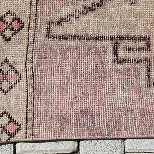 May include: A vintage rug with a pink and beige color scheme. The rug has a geometric pattern with a border of pink and black flowers.