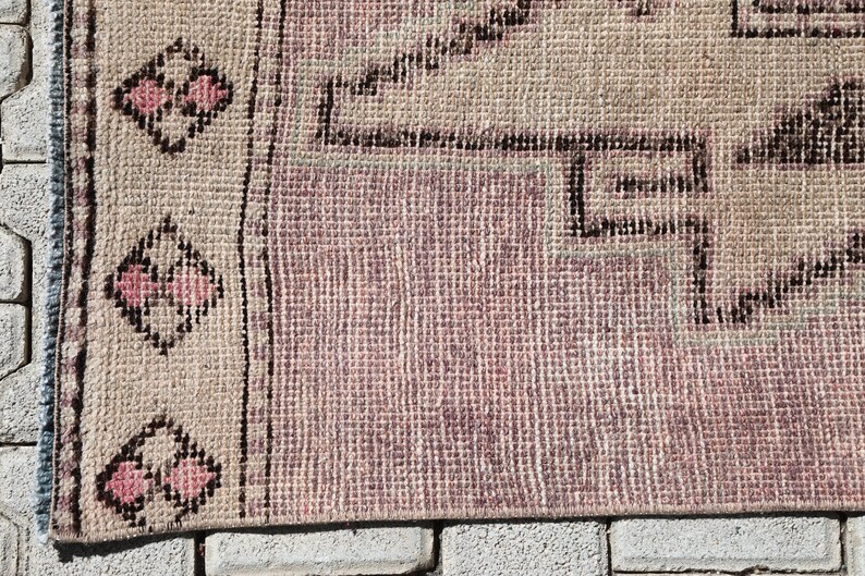 May include: A vintage rug with a pink and beige color scheme. The rug has a geometric pattern with a border of pink and black flowers.