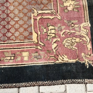 May include: Close-up of the bottom edge of a vintage rug with a dark blue border, a pink and cream center, and a geometric pattern. The rug has a fringe edge.