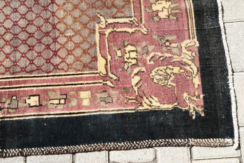May include: Close-up of the bottom edge of a vintage rug with a dark blue border, a pink and cream center, and a geometric pattern. The rug has a fringe edge.