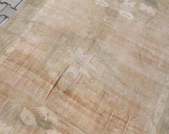 Puede incluir: Una alfombra beige vintage con patrones florales descoloridos y detalles desgastados. La alfombra tiene forma rectangular y un aspecto desgastado, con desgaste visible. La paleta de colores incluye beige, marrón y toques de verde.