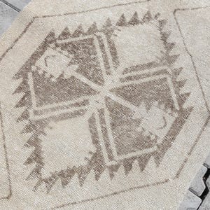 Könnte beinhalten: Beige-brauner Vintage-Teppich mit geometrischem Design. Der Teppich hat eine zentrale Raute mit einem kreuzartigen Muster und einem Dreiecksrand. Der Teppich besteht aus einem gewebten Material.
