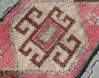 May include: A pink and cream colored rug with a geometric pattern in brown and cream. The rug has a fringe border.