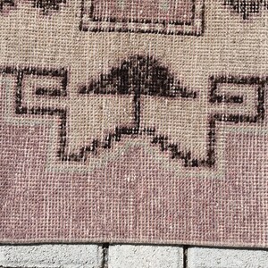 May include: Close-up of a pink and beige woven rug with a black geometric pattern. The rug is made of a soft, textured material and has a fringe border.