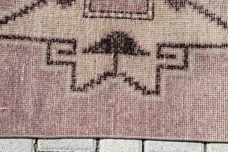 May include: Close-up of a pink and beige woven rug with a black geometric pattern. The rug is made of a soft, textured material and has a fringe border.
