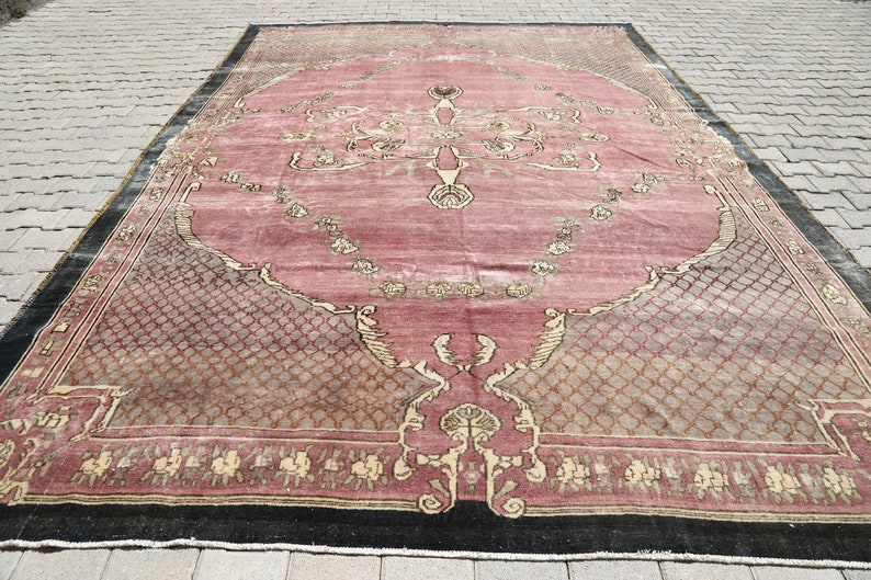 May include: A vintage pink and beige rug with a floral pattern and a black border. The rug has a worn and faded look, giving it a rustic charm.