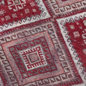 May include: Close-up of a red and beige patterned rug. The rug features geometric designs, including squares and diamond shapes, with a detailed border. The color palette includes shades of red, beige, and gray, creating a vintage aesthetic.