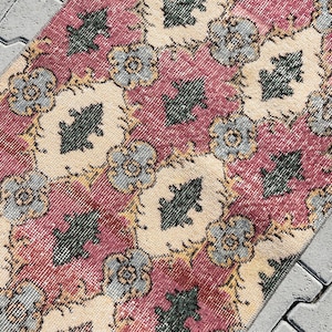 Pode incluir: Um tapete vintage com um padrão floral em tons de rosa, bege e azul. O tapete tem um aspeto desgastado e é feito de um material macio e tecido.