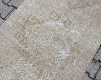May include: A close-up of a beige rug with a faded pattern. The rug has a woven texture and is slightly worn.