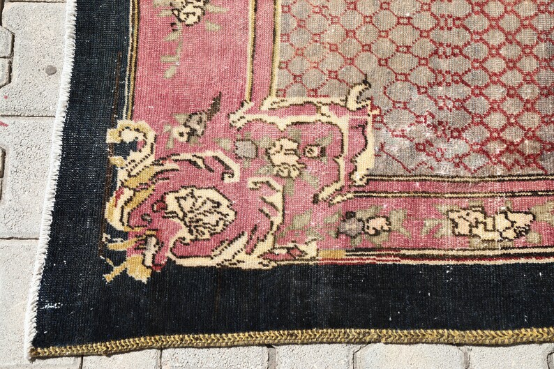 May include: Close-up of a corner of a vintage rug with a black border, a pink and cream floral pattern, and a geometric design in the center.