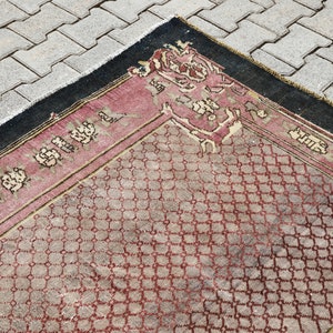 May include: A vintage rug with a geometric pattern in shades of red, beige, and black. The rug has a fringe border and a central medallion.