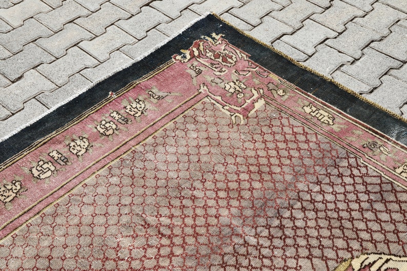 May include: A vintage rug with a geometric pattern in shades of red, beige, and black. The rug has a fringe border and a central medallion.