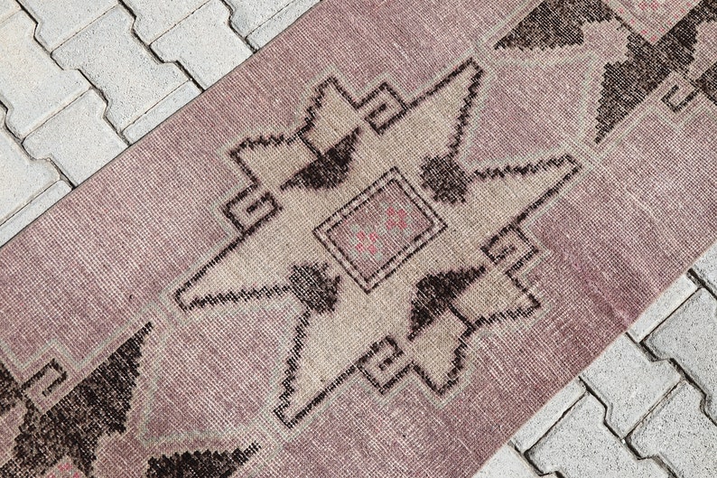 May include: A pink and beige rug with a geometric pattern in black. The rug has a star-shaped design in the center.