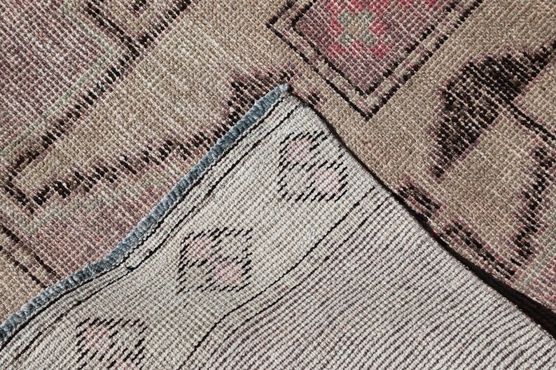 May include: Close-up of a beige and brown woven rug with a geometric pattern. The rug has a blue and white fringe border.