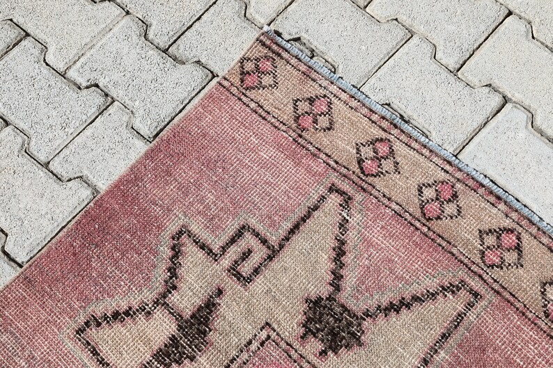 May include: A pink and beige patterned rug with a geometric design. The rug has a frayed edge and is lying on a gray concrete surface.