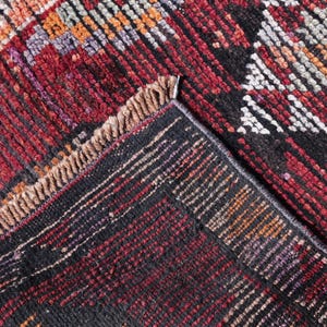 Puede incluir: Primer plano de una alfombra tejida roja, negra y blanca con un patr&oacute;n geom&eacute;trico. La alfombra tiene un borde de flecos.