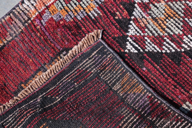 Puede incluir: Primer plano de una alfombra tejida roja, negra y blanca con un patr&oacute;n geom&eacute;trico. La alfombra tiene un borde de flecos.